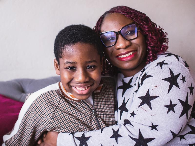 A son and his mother wearing glasses smile, sitting on the sofa together