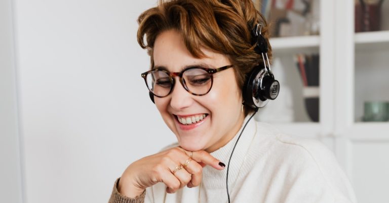 A woman wearing glasses and a headset smiles while sitting at her desk.