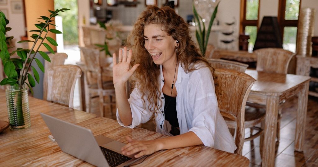 A woman smiles and waves to her colleagues on a laptop while hybrid working.